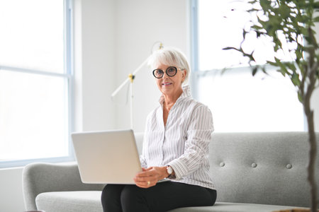 Portrait of elderly woman over grey background sit on sofa with laptop