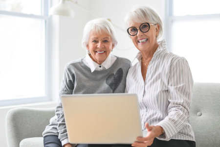 Portrait of two elderly woman sit on sofa at home with laptopの写真素材