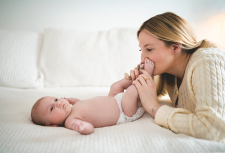 Cute small 1 month baby boy at home. Mother with little newborn infant kiss foot.