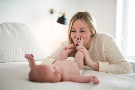 Cute small 1 month baby boy at home. Mother with little newborn infant kiss foot.の写真素材