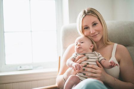 Cute small 1 month baby boy at home. Mother with little newborn infant sit on chair.