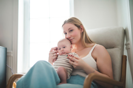 Cute small 1 month baby boy at home. Mother with little newborn infant sit on chair.