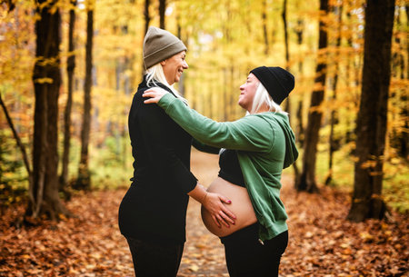 Lesbian couple having fun on autumn forest with futur newborn child on woman belly.の写真素材