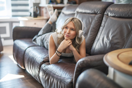 teen listening to music with wireless headphones sitting on a couchの写真素材
