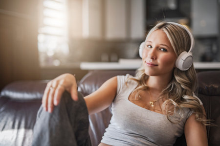 teen listening to music with wireless headphones sitting on a couchの写真素材