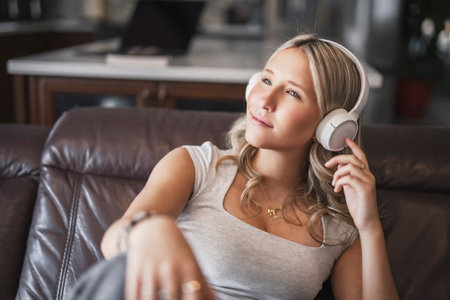 teen listening to music with wireless headphones sitting on a couchの写真素材