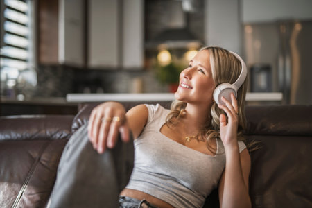 teen listening to music with wireless headphones sitting on a couchの写真素材