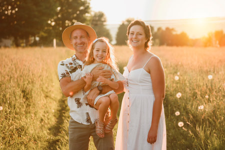 happy child girl and mother and father are playing on field at the sunset