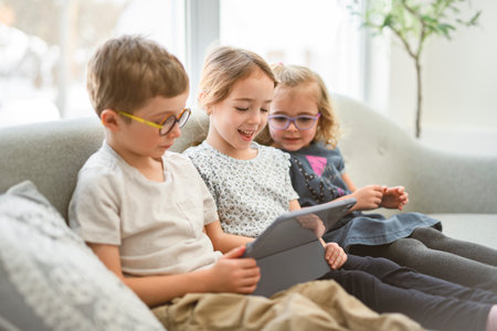 Portrait of a group of children, kids sits on a sofa at home, using tabletの写真素材