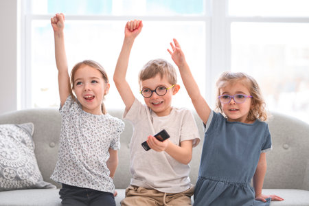 Portrait of a group of children, kids sits on a sofa at home, watching tv together.の写真素材