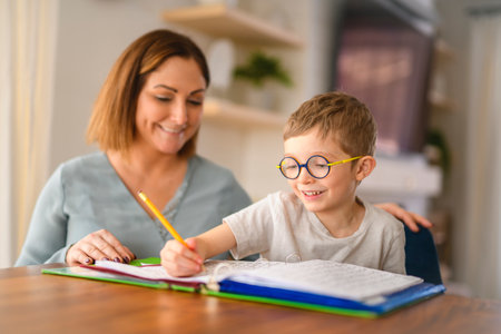 homework and school concept - smiling student boy with book writing to notebook at home with his...