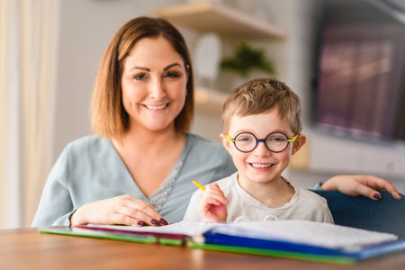 homework and school concept - smiling student boy with book writing to notebook at home with his mother help herの写真素材
