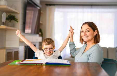 homework and school concept - smiling student boy with book writing to notebook at home with his mother help herの写真素材