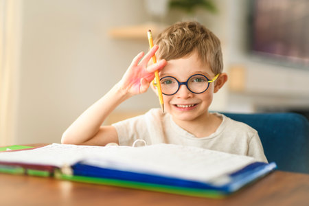 homework and school concept - smiling student boy with book writing to notebook at home