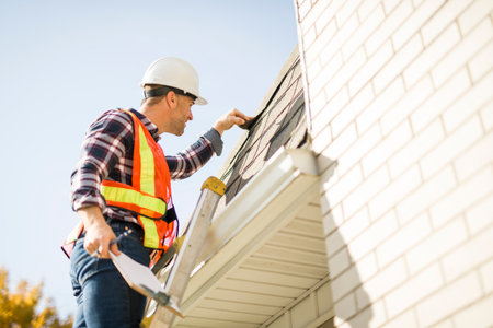 man with hard hat standing on steps inspecting house roofの写真素材