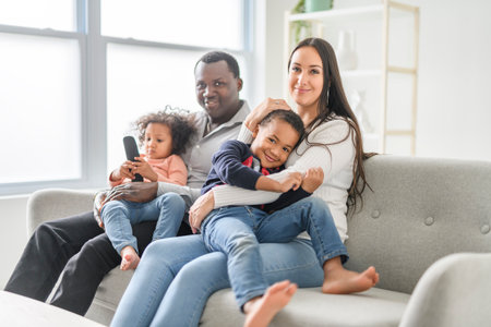 family with boy and girl child posing, sitting on couch and watching tvの写真素材