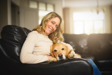 Portrait of woman with healthy golden retriever dog indoors on sofaの写真素材