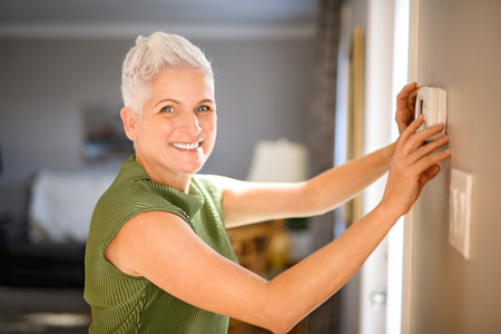 senior lady posing at home portrait close to a window using thermostatの写真素材