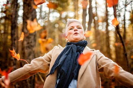 Mature woman in autumn forest, dressed in cozy fall attire, Reflection and connection with nature,...
