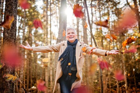 Mature woman in autumn forest, dressed in cozy fall attire, Reflection and connection with nature, wellnessの写真素材