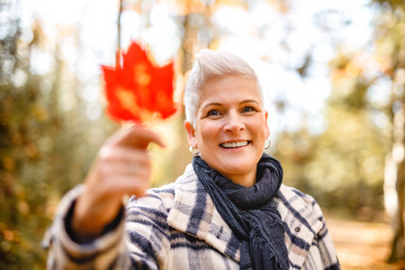 Mature woman in autumn forest, dressed in cozy fall attire, Reflection and connection with nature,...