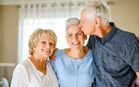 Happy daughter embracing her two elderly parents at living room. Love and care.の写真素材