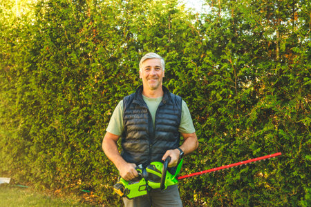 Man worker cutting bushes with an electric saw in the yardの写真素材