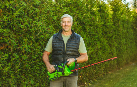 Man worker cutting bushes with an electric saw in the yard