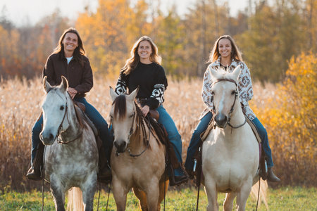 Three young women having a great time with horses in a field during the autumn season at sunset.の写真素材