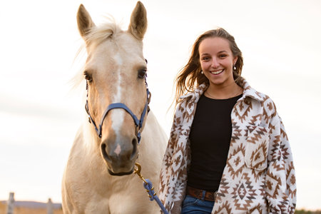 Young woman having great time with a horse in field on autumn season. sunset hour
