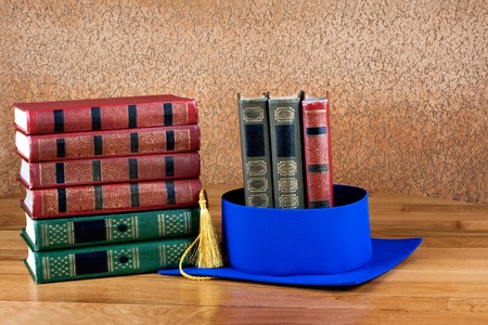 Graduation mortarboard on top of stack of books on abstract background of wallの写真素材