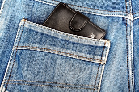 Black leather wallet sticking in the back pocket of denim  blue jeans