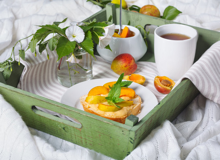 Delicious toasts bread with homemade apricot jam and cup of tea on tray, on background of the flowers of convolvulusの写真素材