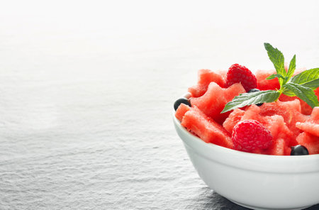 Salad of fresh juicy pieces of watermelon, raspberry and currant with green mint leaves on black stone countertopの写真素材