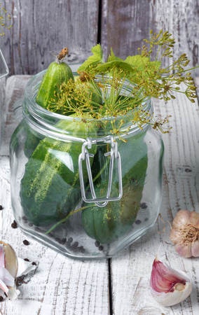 Preserved cucumbers in glass jars with dill, pepper and garlic on wooden tableの写真素材