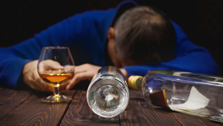 Male alcoholic with glass of whiskey and bottle sleeping on table at night. Alcohol and addiction. Conceptの写真素材