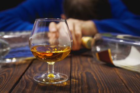 Male alcoholic with glass of whiskey and bottle sleeping on table at night. Alcohol and addiction. Conceptの写真素材