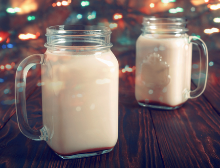 Two glass cups of hot cocoa with milk and sugar, on wooden table, with  festive Christmas lightsの写真素材
