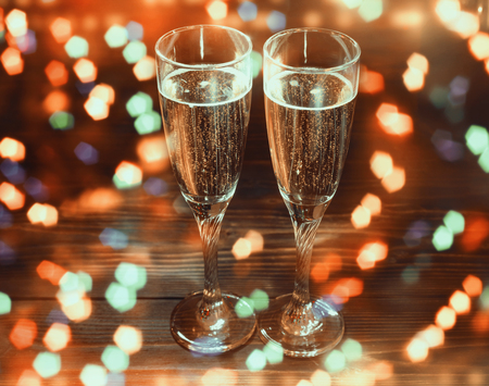 Two glasses of champagne on wooden table in New Year's Eve with bright glitter, lights, blur bokehの写真素材