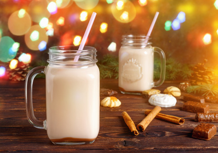 Two glass cups of hot cocoa with milk, cinnamon, candies and  straw tube on background of Christmas fir and cones with blur bokehの写真素材