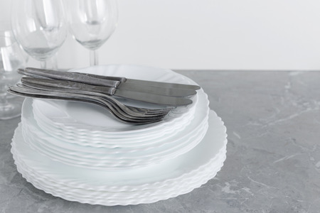 Stack of clean plates with forks, knives and glasses for serving on stone table near the sink