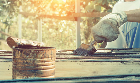Male worker in old glove is painting boards for home decoration in  outdoor