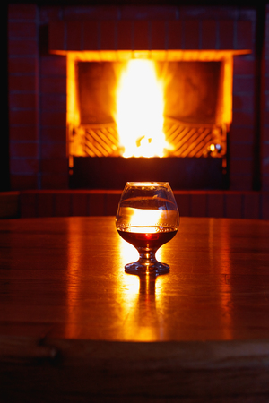 One glass of cognac on background of old brick fireplace with  bright fireの写真素材