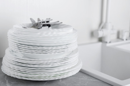Stack of clean plates with forks, knives and glasses for serving on stone table near the sinkの写真素材