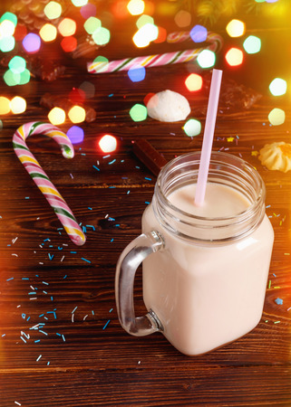 Glass cup of hot cocoa with milk, cinnamon, candies and  straw tube on background of Christmas fir and cones with blur bokehの写真素材