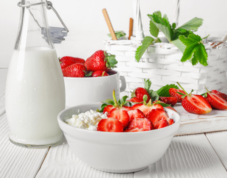 White bowl with fresh red ripe strawberries and natural cottage cheese, on  white wooden table for fitness breakfast.の写真素材