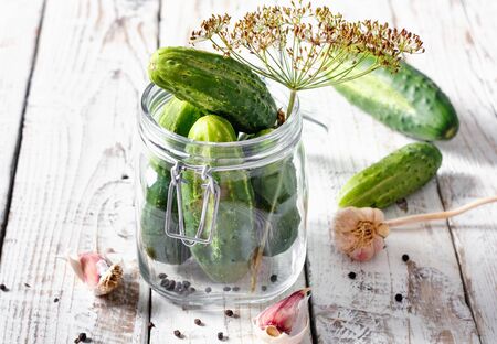 Preserved cucumbers in glass jar with dill and garlic on wooden tableの写真素材