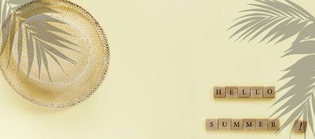 Wooden cubes with text "Hello summer" and fashionable  straw hat  with palm leaves on yellow paper background.
Flat lay, top view, copy space concept.の写真素材
