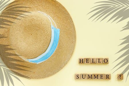Paper beige background with straw hat and blue medical masks. Conceptual text: "Hello summer 2020"  for design. 
 Flat lay, top view, copy space concept.の写真素材