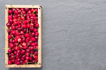 Fresh crop of cherry berries on gray stone countertop, against background of summer greenery. 
Flat lay, top view, copy space concept.の写真素材